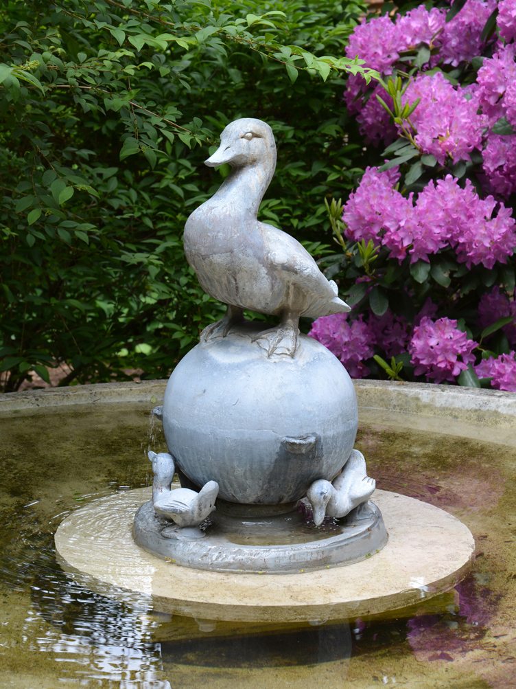 Barbara Israel garden antiques stone duck fountain with purple flowers.
