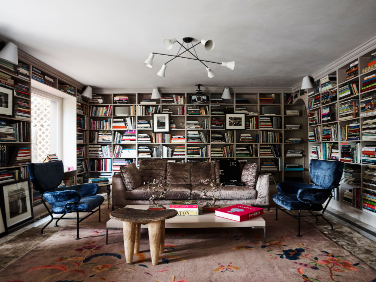 Brigette Romanek's library filled with tomes, two blue crushed velvet accent chairs, a brown velvet sofa, and vintage art and sconces. 