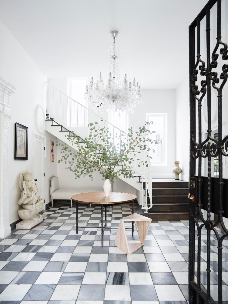 Brigette Romanek's foyer features a round, wooden table, Eastern sculptures, vintage art, and hanging chandelier 