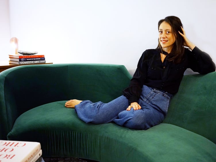 Chiara deRege interior designer sits on a curved velvet emerald couch.