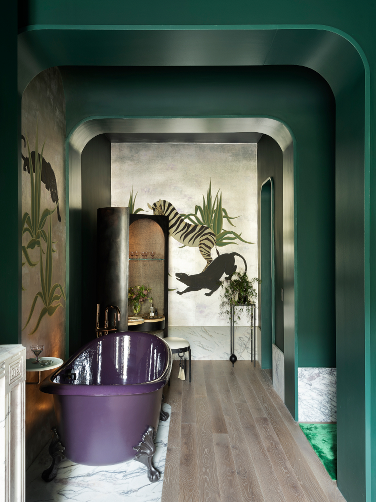 The bathroom features an emerald accent wall, metallic wallpaper, and a purple clawfoot bathtub.