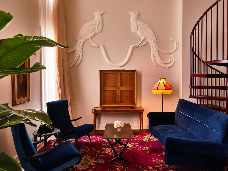 Sitting area with deco blue velvet chairs and couch, spiral staircase, and bird fresco.